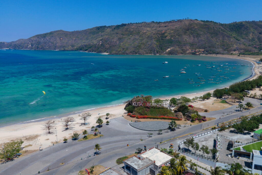 Aerial view of Kuta Mandalika, a coastal area with a white sand beach and turquoise sea, surrounded by hills and featuring a road and several boats in the water—a must-see spot among the things to do in Lombok.