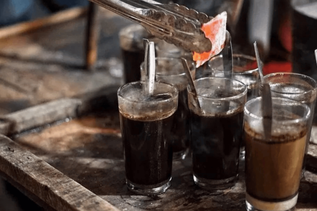 Tongs carefully place hot charcoal into glasses of fragrant black tea, a warm ritual on a wooden table reminiscent of Yogyakarta's rich cultural charm.